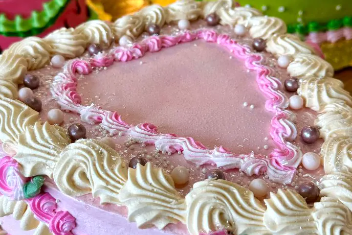 Close-up of a pink heart cake top edged in cream shells, pink piping and sugar pearls.