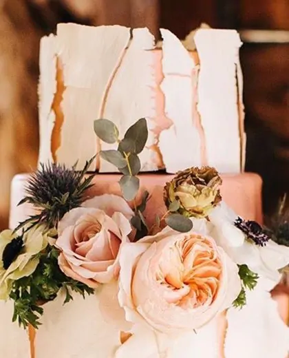 The top tiers of a wedding cake: white shards above a peach tier with roses and thistle.